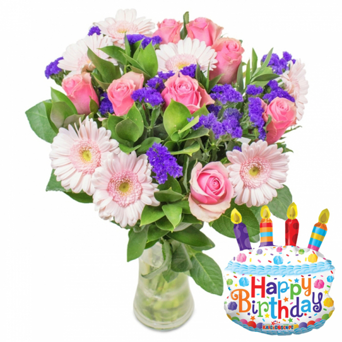 This celebratory arrangement reads like a polished birthday note from a neighbourhood florist: a full bouquet of fresh cut flowers in a simple clear glass vase, paired with a festive, cake-shaped foil balloon that proclaims Happy Birthday. The bouquet's dominant elements are soft pink roses-petals layered and slowly opening from pale blush to a richer pink-paired with large pale-pink Gerbera daisies whose circular faces and subtle yellow-green centres bring a bright, approachable charm. Woven throughout are vivid purple clusters of statice or limonium, their papery texture and concentrated colour producing a lively contrast that gives the arrangement depth and movement. Deep, glossy green foliage frames and supports the blooms, while the clear vase reveals trimmed stems and clean water, a quiet promise of freshness. To the bouquet's right, the white cake balloon, trimmed with blue piping and dotted with colourful sprinkles in red, yellow, blue and green, wears four multi-coloured candles with tiny yellow flames and playful lettering across its face; a discreet KALEIDOSCOPE logo appears on the balloon's lower edge. As a florist who knows New Barnet's streets-from Station Road to nearby Oakleigh Park-I imagine this delivered for a birthday morning on a residential doorstep or presented as a centerpiece at a small family gathering. It balances romantic softness and festive cheer, the kind of thoughtful gift locals choose when they want flowers that feel both familiar and celebratory.