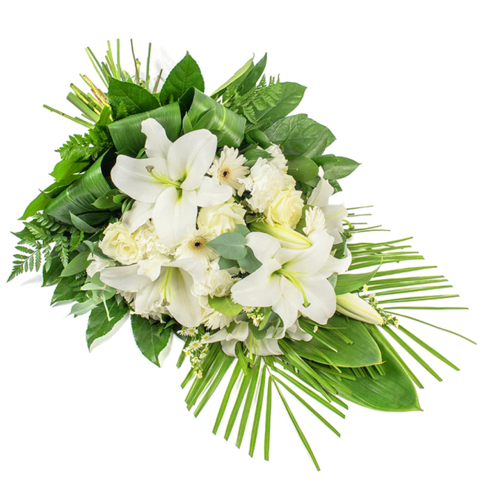 A sophisticated sympathy spray in shades of pure white and rich green is laid out on a pristine white background, designed to be viewed from the front like a floral painting. The arrangement forms an elongated teardrop, flowing diagonally from a generous top left down to a slender point at the lower right. Dominating the centre are several grand white lilies, their trumpet-shaped petals open in full bloom, arching outward and revealing delicate yellow-green stamens within. Some lily buds remain closed, smooth and upright, suggesting continuity and the memory of life carried forward. Interwoven with these are white roses in various stages of opening, from tight buds to layered blossoms, along with ruffled white carnations and clean-petalled Gerbera-style daisies with soft cream or pale yellow centres. Sprays of tiny white filler blooms drift between the larger flowers, adding softness and an almost mist-like texture. Embracing the blooms is a carefully layered collar of greenery: broad, glossy leaves provide deep green contrast; airy fern fronds add a feathery lightness; and rounded eucalyptus leaves in muted blue-green bring a cool, calming undertone. Long leaves are folded into neat, vertical loops near the crown of the design, introducing a tailored, modern detail, while a fan of slender palm fronds unfurls from the base, extending far to the right and accentuating the cascade. The result is a tranquil and dignified tribute that would sit naturally in a New Barnet church or crematorium chapel, its white flowers suggesting purity and peace, and its flowing lines offering a graceful expression of condolence, remembrance, and quiet support for grieving families.