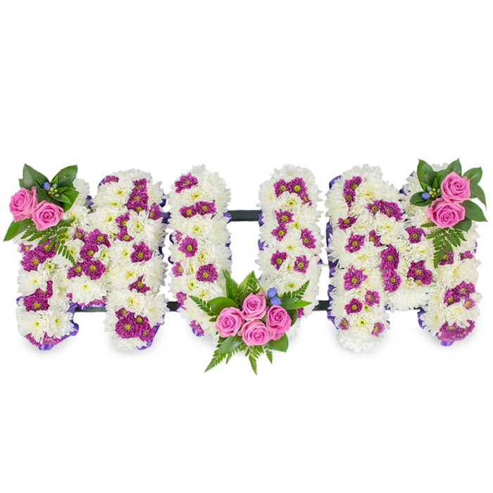 Presented against a simple white backdrop, this bespoke memorial arrangement spells out MUM in bold, three-dimensional letters formed from dense, fluffy white chrysanthemum blooms that appear almost like soft snow. Scattered through the white are concentrated areas of magenta and deep purple spray chrysanthemums, placed to create a gentle pattern that gives each letter a subtle sculpted look. Along the edges of the letters a delicate purple ribbon traces the contours, quietly defining the shape and lending a finishing, respectful flourish. Three clusters of warm pink spray roses provide tender focal points: a delicate pair at the top left of the first M, a larger, luxuriant bouquet nestled in the lower curve of the U, and a matching cluster at the top right of the final M. The roses are cushioned by rich, dark green foliage-fern fronds and mixed leaves-that add a textural counterpoint and a cool, leafy scent, while tiny blue accent flowers peek through the greenery like small, calming stars. A slim, dark support bar runs horizontally to connect the letters and maintain the composition's balance when displayed at a funeral service or memorial reception. The overall tone is one of solemn affection and refined craftsmanship, a traditional sympathy tribute that honours motherhood with quiet beauty. This design reflects the considered workmanship often requested by families in New Barnet and surrounding neighbourhoods when creating a personalised floral farewell.