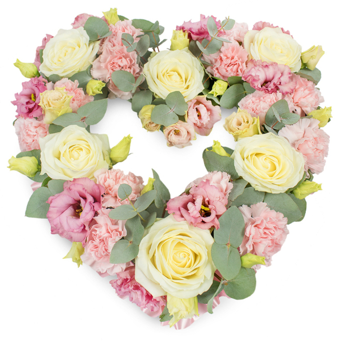 A meticulously crafted heart-shaped tribute dominates a clean white background, its pastel flowers forming a complete, continuous heart that appears both strong and tender. The wreath is lavishly full, with no visible gaps, suggesting expert hands arranging each stem until the outline feels perfectly balanced. Cream and buttery yellow roses are the visual anchors, their spiralling centres and smooth, velvety petals offering a sense of timeless elegance and quiet dignity. Nestled around them are airy clusters of soft pink carnations, every head composed of countless frilled petals that whisper of gentleness and care. Interwoven with these are lisianthus blooms in richer shades of rose, berry-pink, and soft mauve, their slightly more open, layered petals adding an almost romantic note to the design. Threading through the blooms, silvery eucalyptus leaves in muted green tones lend a calm, cool contrast; their rounded shapes and subtle sheen catch the light and echo the natural greenery of New Barnet's tree-lined streets near Hadley Common and High Barnet. Here and there, tiny yellow-green buds peek between the larger flowers, suggesting freshness and the fact that the piece has been created only hours before, ready for delivery to a local chapel, cemetery, or family gathering. The overall colour palette-creams, soft pinks, gentle yellows, and eucalyptus green-creates an atmosphere of peace and remembrance. This heart wreath feels ideal as a funeral or memorial tribute, offering a tender message of love that does not need words. It looks like the kind of design a dedicated New Barnet florist would prepare when a family wishes to honour a life with beauty, comfort, and quiet grace.