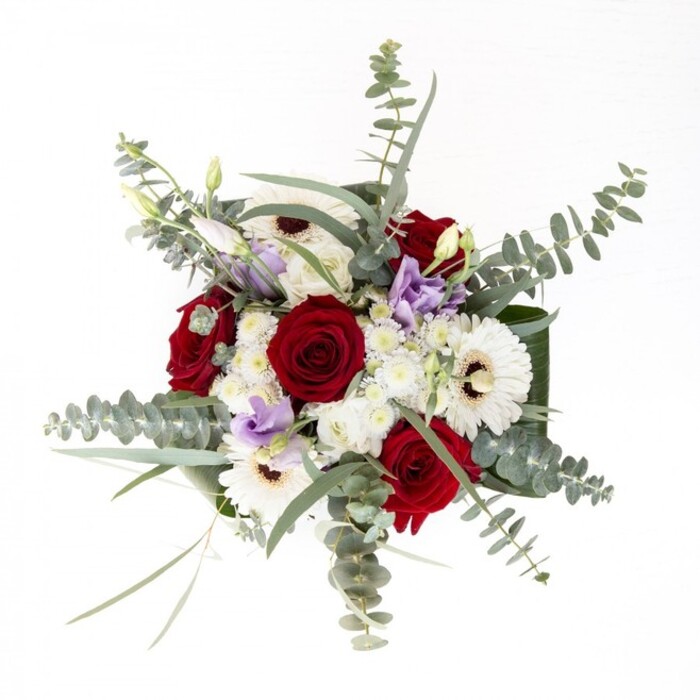 From the experienced hands of a New Barnet florist, this bouquet embodies a harmonious union of sophistication and heartfelt warmth. At the centre, classic red roses anchor the display-a timeless declaration of love, their velvety petals opening slowly in the filtered light. Around them, crisp white gerbera daisies beam with character, their dark centres grounding the arrangement with quiet confidence. Pastel-hued lisianthus, carrying hints of lilac and lavender, meander through the bouquet in stages of bloom, some buds suggesting the anticipation of life's ongoing moments. Soft white filler flowers lend a delicate, frothy texture, reminiscent of spring mornings along East Barnet Road. Eucalyptus leaves fan out with their signature silvery-blue sheen, dispersing a subtle, invigorating scent that quietly uplifts the senses. The sculpted dark green foliage wrapped around the vase's rim gives the bouquet a distinctly polished finish, reminiscent of the carefully maintained gardens of New Barnet. The interplay of lushness, vivid hues, and artful arrangement makes this bouquet ideal for occasions spanning joyful celebrations to dignified sympathy. Whether gracing a tea table near New Barnet station or adding serenity to a modern flat overlooking local parks, this composition is a statement of fresh beauty, skilled craftsmanship, and a deep understanding of what brings joy and comfort to the New Barnet community.