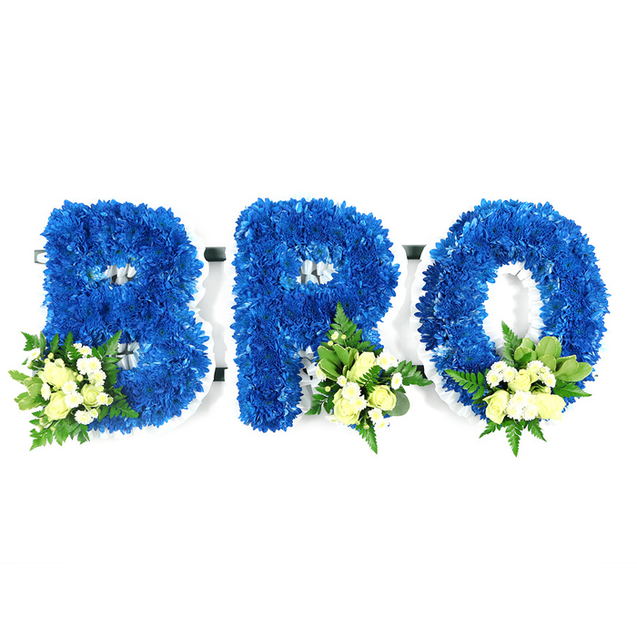 A carefully composed studio shot shows a three-piece funeral tribute spelling BRO, each capital letter built from tightly packed royal blue chrysanthemums that give the lettering a plush, velvet-like texture. The image is lit evenly against a stark white background so the white foam frame beneath the flowers is faintly visible around the B's curves, the R's leg and the O's centre, revealing the structural care beneath the lush blooms. Each letter carries a small cluster of accents placed with deliberate symmetry: the B's cluster at its lower-left curve, and the R and O clusters near their lower-right bases. These accents include pale cream or ivory spray roses - some still coyly budded, others showing soft petals - mingled with tiny white filler flowers and a selection of greens ranging from glossy broad leaves to delicate, fern-like fronds. The result is a refined contrast of saturated blue and gentle ivory tones, a composition that reads as both bold and consoling. As a New Barnet florist I often prepare similar tributes for local families attending services near Monken Hadley Common, Barnet High Street chapels or the quiet corners beside Brunswick Park; Flowers New Barnet crafts these pieces with the sensitivity such moments require and can arrange local delivery when requested. This arrangement's visual language - the striking blue for remembrance tempered by creamy accents and green texture - offers a dignified, heartfelt way to honour a brother or close friend at a funeral, graveside or memorial gathering.