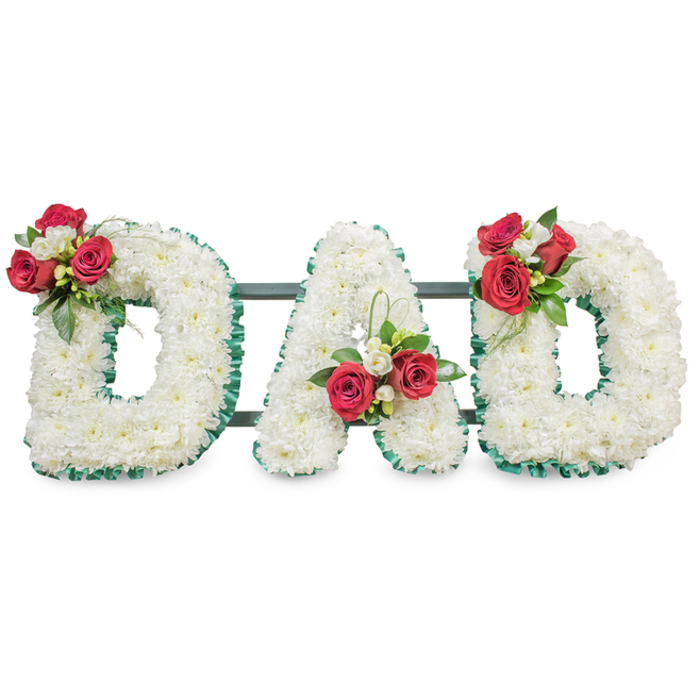 A poignant, meticulously arranged tribute spells the word DAD in large block letters, each letter densely packed with small, pristine white chrysanthemum blooms that produce a uniformly soft and reverent surface against a bright white backdrop. The edges of each letter are finished with a vivid emerald-green ribbed ribbon that crisply defines the shapes and gives a formal, dignified outline. On the upper left curve of the first D there is a striking cluster composed of deep red roses, smaller white freesia and abundant dark green foliage; the A carries a near-identical cluster positioned toward its lower left stem, accented by a slender loop of bright green bear grass that arcs upwards; the final D mirrors the first with a corresponding arrangement of red roses, white freesia and lush leaves. Between and behind the letters, slim dark green or black support bars are discreetly visible, engineered to secure the composition for placement on a chapel stand or graveside easel. The lighting is soft and even, allowing the velvety texture of the rose petals and the fine detail of the chrysanthemum florets to be clearly read without harsh shadow. The scent suggestion - the faint citrus-honey of freesia and the classic, warm perfume of red roses - gives the tribute a quietly comforting presence. This classic sympathy design, suitable for memorials and funeral services across New Barnet and neighbouring Hadley Wood or Oak Hill Park, combines symbolism and craftsmanship: white chrysanthemums for devoted love and red roses for enduring respect, composed with measured restraint and heartfelt intention.
