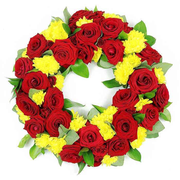 Displayed against a clean white backdrop, this circular floral wreath appears full and substantial, a traditional funeral tribute crafted with great attention to detail. The body of the wreath is densely covered with deep red roses and cheerful yellow chrysanthemums, creating a strong visual contrast that feels both warm and dignified. The roses dominate the design, each bloom fully open and carefully placed so that their velvety petals create a rich, layered surface. Some roses lean more towards a classic crimson, while others carry a slightly darker, burgundy hue, giving the ring a subtle play of light and shadow. Interspersed between them are clusters of bright yellow chrysanthemums, likely small spray or button varieties, their many fine petals fanning out in soft, cushiony mounds. These yellow flowers introduce a sense of lightness and hope, gently lifting the more intense tones of the red roses. Tucked throughout the arrangement is a foundation of fresh green foliage, including shiny, mid-green leaves reminiscent of salal and perhaps some softer, cooler-toned sprigs that suggest eucalyptus. This greenery adds structure, depth, and a natural frame to the blooms, hinting at professional floristry skills often found in established New Barnet flower shops. The open centre of the wreath is clearly visible, reinforcing its symbolism of eternity, continuity, and ongoing remembrance. Bright, even photography lighting highlights the vivid colours, crisp edges, and the slight gloss of some leaves without creating strong shadows. The overall impression is of a high-quality sympathy wreath, suitable for funerals, memorial services, or graveside tributes around New Barnet and nearby communities, conveying deep love, gratitude, and a respectful farewell.