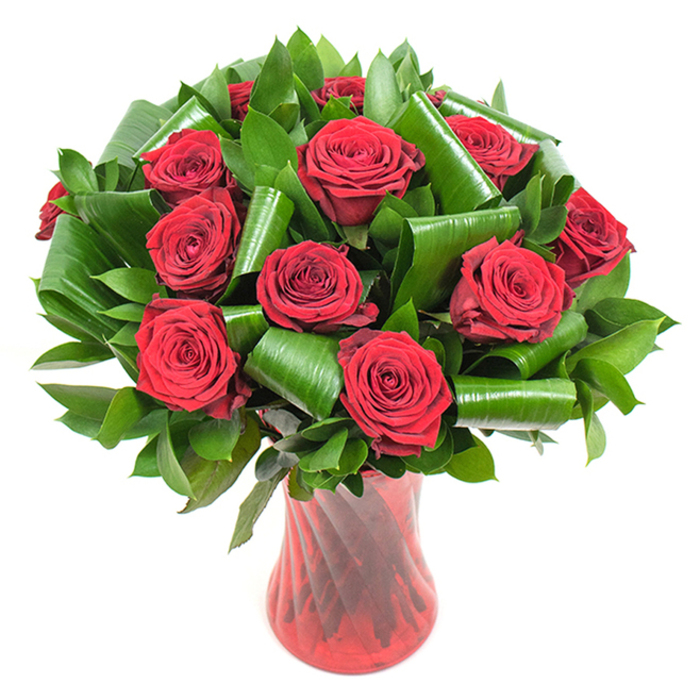 A dramatic, carefully balanced bouquet of deep crimson roses takes centre stage, each rose opened into a full, velvety bloom whose petals fold tightly into classic spirals and reflect a rich, wine-coloured depth. The overall shape is a lush dome, the individual heads packed closely so that the texture reads as a single, sumptuous surface. Interwoven throughout are layers of dark green foliage: smaller, glossy greens that provide a dense, verdant foundation, and larger, shiny leaves that have been artfully rolled and curved into refined loops and spirals. These broader leaves add sculptural rhythm and a contemporary edge, cradling the rose heads and creating visually intriguing negative space between blooms.

The flowers are housed in a tall, translucent ruby-red glass vase with a subtle ribbed or twisted finish, the surface catching vertical highlights and reinforcing the bouquet's elegant silhouette. Against a plain white backdrop the reds and greens appear vivid and immediate, and the soft, even lighting highlights surface texture-the velvet of the petals, the sheen of the foliage, the glossy glass of the vase. Speaking as a local florist, this arrangement reads as a classic expression of passion and celebration: appropriate for anniversaries, Valentine's, romantic surprises, or as a sophisticated centrepiece for an intimate gathering. Crafted with attention to balance, scent, and longevity, it's a design that travels well for delivery across New Barnet and the nearby borough, promising fresh, tactile beauty on arrival.