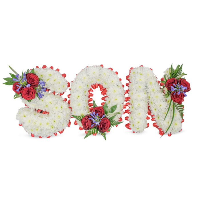 A poignant, carefully crafted tribute spells SON in large three-dimensional letters, placed against a simple white field that emphasises the arrangement's solemn clarity. Each character is built from a dense coat of pure white spray chrysanthemums, their tiny rounded blooms packed so closely the letters appear soft and seamless, like stitched clouds. The perimeter of each letter is defined by a striking red satin ribbon, pleated into a scalloped border that neatly hugs the contours of the S, O and N and brings a formal, respectful contrast to the white. Tasteful clusters sit at three points to lend colour and emotional weight: the upper left of the S carries a grouping of velvety deep red roses, interspersed with spiky blue-purple stems resembling Liatris and swathes of dark green fern and trailing foliage; the O is similarly adorned at its lower centre, and the N receives a cluster on its top-right flank that cascades slightly down the stem. The roses introduce a warm, velour texture against the chrysanthemums' soft billow, while the vertical spikes add a contemporary, upward energy. Soft studio or morning light sculpts the forms, casting minimal shadow so the focus remains on colour and texture. This personalised floral lettering expresses purity, grief, and steadfast love - symbolism families in New Barnet often choose for memorials at local funeral homes or at services near Hadley Green - and it communicates careful workmanship intended to honour a beloved son with dignity and heartfelt remembrance.