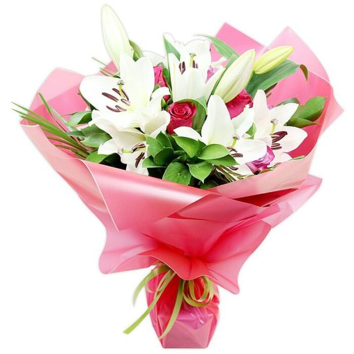 A striking bouquet of pristine white lilies and deep red roses is photographed against a minimalist white backdrop, creating a sense of calm that lets the colours and forms of the flowers truly sing. The focal point is a cluster of large, fully open white Oriental lilies, each bloom shaped like an elegant trumpet, with petals that curl outwards and slightly backwards, revealing pale veining and a satiny texture. At the centre of each lily, prominent stamens carry dark, reddish-brown anthers, some already dusting the inner petals with a hint of pollen, while the pistils extend gracefully forward. Surrounding these open lilies are several firm buds, tipped with green and cream, hinting at more flowers yet to open and extending the life of the arrangement. Between the lilies, groups of deep red roses provide a rich, romantic contrast. Some roses are tight, perfectly formed buds with a velvety matte finish, while others are beginning to open, their layered petals forming classic cup shapes. The blossoms are supported by abundant foliage: deep green, glossy leaves and narrower, grass-like strands that weave through the bouquet, adding depth, texture, and a slightly wild edge reminiscent of the greenery seen in gardens near Victoria Park and residential streets around New Barnet. All the stems are gathered neatly and wrapped in an ample swathe of bright pink, semi-translucent cellophane or floral paper, which fans out around the flowers in ruffled folds that catch the light and add a celebratory energy. At the base, a slim lime green satin ribbon is tied in a simple bow, its delicate sheen and fresh hue echoing the natural stems beneath. The arrangement feels both elegant and joyful, ideal for thoughtful gifting, from anniversaries and birthdays to well-wishes for neighbours across New Barnet.
