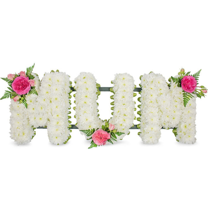 This photograph captures a carefully arranged MUM funeral tribute, designed in the classic style much loved by families in New Barnet and the surrounding suburbs. Three tall block letters stand side by side, clearly legible and evenly spaced, their shapes defined entirely by small white spray chrysanthemums. Every bloom sits tightly against its neighbours, creating a continuous blanket of white that looks almost like freshly fallen snow, smooth and serene, with just the tiniest hints of yellow-green at the flower centres. A narrow edge of dark green ribbon follows the contours of each letter along the base, slightly glossy in the light and supported by a hidden metal frame that ensures the tribute stands firm during the funeral service or while being carried from a local church to the crematorium. To break the whiteness and add emotional depth, the florist has placed three coordinated flower groupings. On the upper left arm of the first M, a lush fuchsia garden rose is the focal point, surrounded by soft pink spray roses and tightly closed buds, all cushioned against the chrysanthemums. The bottom curve of the U holds another similar cluster, positioned so it feels like a gentle hand at the heart of the word, and a final matching spray balances the top right of the second M. Delicate fern leaves and fresh foliage extend beyond each cluster, giving movement and a touch of garden-like grace. The composition conveys a sense of peaceful remembrance, suitable for same-day delivery to services across New Barnet, whether at a quiet chapel, a family home, or a graveside farewell for a much-loved mum.