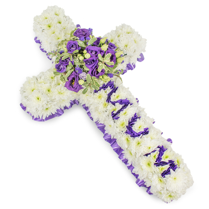 An elegantly composed, large floral cross fashioned from dense clusters of snow-white chrysanthemums, their rounded florets tessellated to form a seamless, cushion-like face that speaks of purity and peace. The whole shape is traced by a rich purple satin ribbon, pleated and folded to produce a ruffled border that reads formal and respectful against the white blooms. In the centre a lavish spray creates the focal point: deep violet roses and paler lavender roses sit alongside ruffled lisianthus (eustoma), the interplay of dark and pale purples producing visual depth and a quiet, dignified drama. Variegated greenery - pale-edged, darker-centred leaves suggestive of pittosporum - gives the bouquet structure and a gentle, natural rhythm, while small green berries are tucked through the cluster to add subtle texture. Along the vertical stem the letters MUM appear in carefully placed purple flower heads, each letter distinct and heartfelt against the white chrysanthemum field, making the tribute unmistakably personal. The composition is photographed against a stark white background with soft, even lighting that makes the violets sing and the whites look luminous; one can almost feel the plush density of the petals and the satiny touch of the ribbon. As a florist who prepares tributes for wakes and services across New Barnet, from Brunswick Park to Barnet High Street, I select these cool, comforting tones and compact workmanship to offer a message of respect, memory and peaceful farewell.