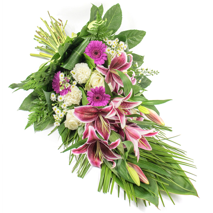 An elegant funeral spray is displayed against a clear white backdrop, its diagonal composition guiding the eye from the bound stems at the upper left down to a graceful point at the lower right, creating a gentle crescent shape filled with colour and meaning. Dominating the arrangement are several striking Stargazer lilies, their wide, star-shaped petals a deep fuchsia-pink with sharply defined white edges and a scattering of burgundy spots that add depth and drama. Some lilies are fully opened in their prime, while others remain in slender buds tinged with pink and green, suggesting both cherished memories and the continuity of life. Clustered amongst them are magenta gerbera daisies with bold central disks, lending a vivid, cheerful echo to the otherwise tranquil palette. Soft white roses, some still tightly closed, nestle beside ruffled white carnations, their creamy tones and gentle textures symbolising peace, innocence, and heartfelt respect. Fine clusters of tiny white daisy-like flowers thread through the composition, filling spaces with a subtle, cloud-like lightness. The blooms are embraced by abundant foliage: glossy dark green leaves form a solid foundation, framing the flowers, while feathery ferns and long, arching blades of greenery sweep outwards and downwards, accentuating the sheaf's elongated shape. The overall look is lush yet composed, a blend of vibrant pinks and calm whites supported by deep green tones. Crafted by an experienced local florist for families in New Barnet and the surrounding Barnet and Hadley areas, this tribute feels both personal and dignified, suitable for laying at a graveside, accompanying a coffin, or sending as a thoughtful expression of sympathy to those in mourning.
