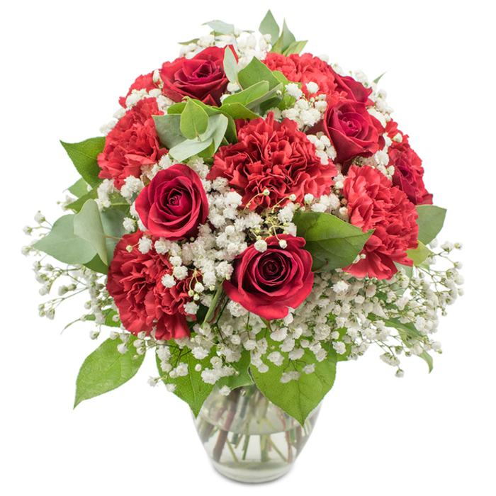 A richly romantic bouquet of red and white flowers is displayed in a clear glass vase, set against a bright white backdrop that allows the colours to sing, as if ready to be delivered to a doorstep in New Barnet. The dominant blooms are deep, velvety red roses, their petals spiralling inward with that familiar classic rose form that speaks of enduring affection and heartfelt sentiment. Around and between them, generously sized crimson carnations provide a lush, ruffled texture; their many layered petals catch the light in soft ripples, making the arrangement appear full and luxurious from every angle. Threaded through the ruby tones are generous sprays of pure white baby's breath, each tiny flower forming part of a delicate cloud that lifts and softens the whole design, creating a gentle contrast against the bold reds. Various shades of greenery provide a fresh, natural frame: the rich dark leaves of the roses mingle with rounded, silvery eucalyptus foliage, adding subtle colour shifts and a slightly modern twist to this otherwise timeless composition. The bouquet is crafted into a rounded, domed shape, expertly balanced so the eye moves easily from rose to carnation to baby's breath without interruption, like following the curve of a quiet walk from New Barnet towards Monken Hadley Common. The transparent vase is simple, with a softly flared lip and clear, clean water cradling the neatly trimmed stems, adding to the sense of freshness. This arrangement exudes warmth, passion, and quiet elegance, ideal as a romantic dinner centrepiece in a New Barnet home, a surprise anniversary gift, or a thoughtful gesture sent to a loved one near Oakleigh Park.