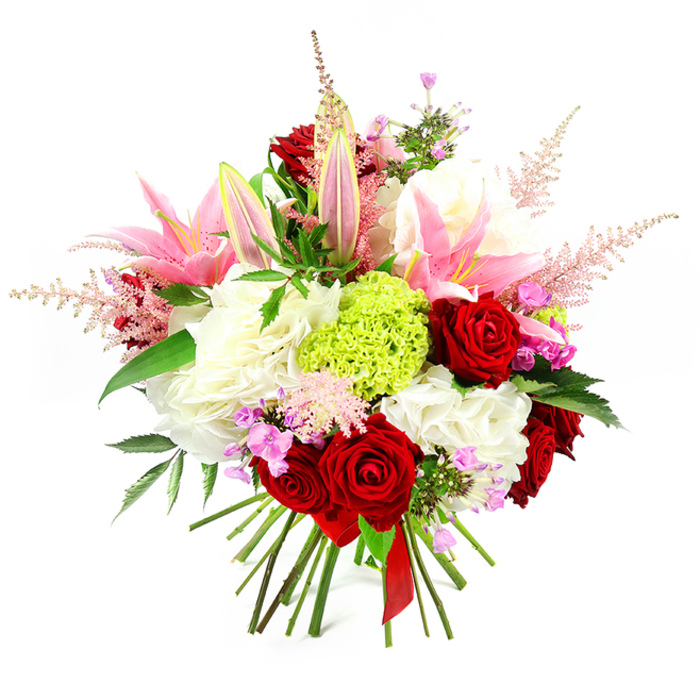 A dense, opulent hand-tied arrangement presented against a clean white backdrop, this bouquet balances classic romance with a contemporary twist-ideal for gifting around New Barnet or for a refined table centre. Dominant crimson roses, each with velvety, spiralled petals, form deep, passionate focal points across the bouquet, their weight steadying the composition. Pink lilies with broad, softly curved petals emerge prominently from the upper plane; some are fully open, revealing pale throats and delicate stamens, while others linger as elongated buds that promise unfolding fragrance. Generous clusters of ruffled white blooms-suggestive of garden roses or large carnations-create a creamy, cloud-like mass that adds both volume and a plush textural counterpoint. A central mound of lime green textured florets, likely a Green Trick carnation or similarly compact viburnum, provides an eye-catching burst of verdant colour and unusual surface interest. Pale pink astilbe sprays extend outward to soften the silhouette and lend an airy, whimsical quality, while scattered fuchsia and lavender filler flowers punctuate shadowed areas, enriching the tonal range. Deep green glossy foliage peeks through, framing the flowers and enhancing contrast. The stems are gathered with professional precision and tied with a single elegant red satin ribbon, the hand-tied presentation signaling thoughtful craftsmanship. The overall effect is celebratory and sophisticated, evoking quiet joy and tactile beauty-an excellent choice for Valentine's gestures, Mother's Day surprises, anniversary bouquets, or a special delivery across New Barnet to homes and offices near Victoria Recreation Ground and Station Road.