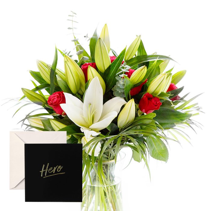 With a joyful hand, I blend bold with serene to honor strength and grace. White lilies drift at the heart of the bouquet, luminous and airy, their satin petals contrasting splendidly with the tactile, lush greenery that encircles them. Rich ruby roses punctuate the design, each bloom a symbol of love and respect. The verdant leaves provide a cooling, forest-like backdrop, while unopened lily buds suggest anticipation and new beginnings. In soft, natural light, the arrangement feels alive and uplifting-perfect for honoring someone's power or celebrating a significant achievement. The accompanying Hero card makes the gesture intimate and enduring. This creation by Flowers New Barnet sits well on a dining table in a home near New Barnet High Street or beside a kitchen window in a sunlit EN5 flat, ready for same-day delivery to brighten a milestone or moment of recognition. The bouquet's structure-hand-tied, with generous stems and generous greens-speaks to the craft of a local florist who understands how colour and texture work together to inspire pride.