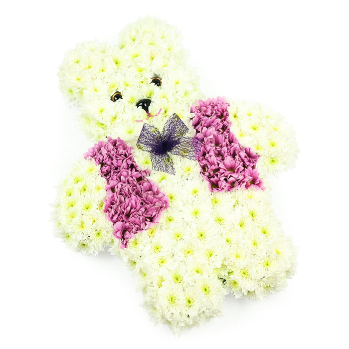 In this tender floral tribute, a teddy bear figure crafted from hundreds of chrysanthemums seems to sit quietly in a pool of soft white light. The bear's entire form is shaped with creamy white, slightly feathery petals, packed so closely that the surface appears velvety and inviting to the touch, just like a favourite soft toy. Its head is pleasingly round, the ears carefully domed and distinct, and the body proportioned with plump arms and legs that create a sense of security and comfort. Two dark, glossy eyes and a neat black nose introduce just enough contrast to bring the face to life, giving the impression that the bear is gently watching over someone dear. A suggestion of a curved mouth beneath the nose adds to its kind, reassuring expression. Across the chest, a waistcoat effect is created using a deeper band of magenta and rosy-toned blossoms, the colour rich but not overpowering, symbolising love held close to the heart. At the top of this floral waistcoat, a small bow of sheer violet netting rests at the neckline, catching the light and adding a delicate, almost storybook charm. The plain white background ensures that every nuance of the flowers stands out clearly-the soft creams, the bright pinks, the touch of purple. This is the sort of thoughtful arrangement a family in New Barnet might choose when arranging a child's farewell, a christening remembrance, or a gentle tribute for a little one at a chapel near Victoria Park, allowing flowers to say what voices sometimes cannot.