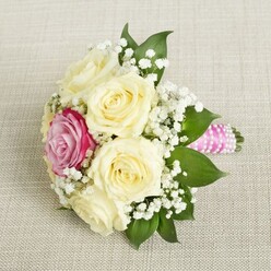 Imagine waking in New Barnet to the promise of a special day-a delicate bridal or bridesmaid bouquet lying on a pale, textured linen, illuminated by the soft yellow glow peeking through a north-facing window. This intimate arrangement showcases lush cream roses, each blossom at its fullest, exuding a gentle perfume that mingles with the sweet, crisp air often found strolling through Oakhill Park in spring. In their midst, a singular magenta-pink rose draws the eye, its hue alive and celebratory, perfectly offsetting the tranquil palette. Scatterings of ethereal white baby's breath drift between the roses and the fresh, emerald green foliage, lending a romantic, almost whimsical quality as if capturing the spirit of a New Barnet garden in bloom. The stems, bound tight with vivid pink satin ribbon and circled by glimmering pearls, evoke memories of thoughtful preparation and attention to detail. This bouquet, resting quietly yet confidently, seems to whisper of new beginnings, heartfelt vows, and joyful moments shared locally-from a sunny wedding at Christ Church to anniversary surprises delivered across Barnet fields. The arrangement speaks not only of beauty and romance, but of the artistry of local florists who infuse every petal with genuine care and a sense of place.