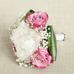In this New Barnet-inspired bridal bouquet, classic romance and local elegance intertwine. The eye is first drawn to two lush pink roses, their petals spiralling open with a gentle transition from passionate fuchsia at the edge to soft blush and lavender at their heart-each rose embodying a sense of excitement and tender hope that mirrors joyful celebrations at places like Victoria Park or Brookhill Road. Set between them is a standout, generously bloomed white peony, its layers of silky, ruffled petals creating a cushion of creamy softness that seems to glow beneath ambient, welcoming light. Throughout the bouquet, sprigs of dainty white gypsophila scatter like stardust, filling the design with a light, cloud-like effect that is both ethereal and grounding. The composition is expertly encircled with sturdy, deep green leaves-possibly ti or aspidistra-folded to cradle and amplify the vibrance of the florals. A snowy white satin ribbon elegantly encases the stems, making it easy to envision this arrangement gracing the hands of a bride or loved one along the avenues of New Barnet. The subtle, fresh fragrance mingles with the soft textures in a harmony that feels at once celebratory and reflective-a bouquet crafted not just for weddings, but for any milestone or sentimental offering within the community. This is a true testament to the artistry and warmth of your local New Barnet florists.
