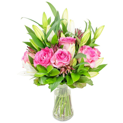 An elegant floral study in pink and white, arranged by Flowers New Barnet with confidence and care and photographed on a pristine white background. The composition centers on several fully opened deep-pink roses whose silky petals graduate from pale blush at the edges to a concentrated fuchsia in the heart, suggesting a soft, lingering fragrance that fills the room. Interlaced among the roses are white lily buds in varied stages - some closed like little promises, others beginning to bloom and reveal the lily's classic trumpet curve - adding height and a sculptural rhythm to the bouquet. A generous framework of green foliage, mixing broad glossy leaves and slender, airy sprigs, creates a verdant stage that makes the pinks and whites sing; darker reddish-brown accent buds are threaded through the greens, adding subtle depth and a natural, garden-like texture. The clear glass vase, slightly tapered at the base, holds fresh water through which the straight green stems are visible, a quiet testament to careful trimming and presentation. The clean, bright lighting highlights petal veins and leaf sheen, conveying freshness ideal for a special occasion or same-day delivery around New Barnet, whether to a home near the station or to a neighbour on Station Road. This bouquet is composed to read as both celebratory and tender - a tasteful choice for Mother's Day, an anniversary, or a heartfelt gesture to lift someone's afternoon.