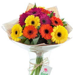 Bursting with colour and crafted with passion by a New Barnet florist, this striking bouquet of Gerbera daisies offers a visual feast for the senses. Vibrant sunny yellow, bold tangerine orange, and rich magenta flowers cluster together atop slender, freshly cut stems, their turned-up faces capturing the cheerful mood found in New Barnet's bustling weekend markets. The arrangement is artfully tied and cocooned in natural brown kraft paper, which brings a rustic note and a sense of nostalgia, recalling leisurely strolls through Oakhill Park in spring. A glossy cellophane wrap overlays the paper, protecting the bouquet while allowing the multicolored blooms and vivid green foliage to shine with a gentle sheen under soft, natural light. The slender glass vase is filled with clear water, offering a glimpse of every neatly gathered stem-each tied together with a fine band of twine and hung with a tidy white gift tag, discreetly marked with a graceful red rose illustration. This bouquet, reflective of both celebration and gratitude, makes a thoughtful gift for milestones, thank-yous, or for bringing a dose of brightness to a loved one's home in the heart of New Barnet. Every element-form, colour, and texture-speaks to the artisan craftsmanship and local character that define this floral arrangement.