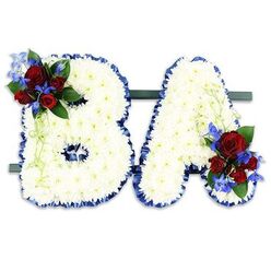An intimate, hand-crafted memorial spells out the initials B and A in bold uppercase forms, each letter densely cloaked in hundreds of small, immaculate white chrysanthemums that produce a soft, textured plane reminiscent of fresh snowfall. The chrysanthemums' layered petals create a gentle cushion that both invites touch and conveys purity, while the subtle floral perfume remains unobtrusive and consoling. The edges of both letters are neatly finished with a ruffled royal blue satin ribbon whose cool sheen sharply frames the white blooms and lends a ceremonial edge. Placed on a discreet dark green rectangular stand, the two letters sit side-by-side as a unified tribute. Floral accents are deliberately mirrored: a compact spray of deep red roses-velvety, passionate, and variously unfurled-sits on the B's upper left curve, balanced by a matching cluster at the A's lower right. Bright cobalt delphinium-like spikes thread through the red roses, their electric blue tones lifting the palette and drawing the eye, while soft, pale green trailing foliage and darker leaves add movement and a living softness. From the perspective of an experienced local arranger who often supplies tributes for services around Station Road and the churches near Oakleigh Park, this piece reads as both personal and dignified-an emblem of respect, a final naming in bloom that comforts family and honors memory with considered colour and form.