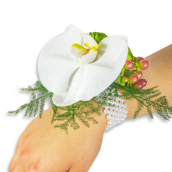 A quiet study in refined contrasts sits on a wrist photographed against a clean white field: a large white Phalaenopsis orchid forms the heart of the corsage, its broad petals smooth and cool to the touch, while a bright yellow labellum with deeper orange tones provides a small, warm focal point. Surrounding the bloom, delicate asparagus fern extends soft, feathery greenery that both cushions and elevates the orchid, creating depth and a gentle halo of verdant texture. Nestled to the upper right is a compact cluster of Hypericum berries, their glossy skins ranging from pale green through rose to a deep crimson-an intentional gradation that reads like the seasons passing in miniature. A little ruffled lime-green foliage adds a crisp accent beside the berries, catching the light with a playful sheen. The arrangement is fastened by a graceful multi-strand pearl bracelet; tiny white pearls wrap comfortably around the wrist, lending a touch of vintage poise and tactile contrast to petals and foliage. The image is lit with soft, diffused daylight that emphasizes natural colours and the craftsmanship of the assemble-orchid's satiny finish, fern's filigree, berry's enamel shine-without distraction. As a local floral piece suitable for weddings, proms, or special ceremonies, it evokes small moments in New Barnet life: a stroll near New Barnet station, a rehearsal dinner at a nearby hall, or picking up bespoke work from a trusted neighbourhood florist. The overall impression is elegant, understated, and composed with care.