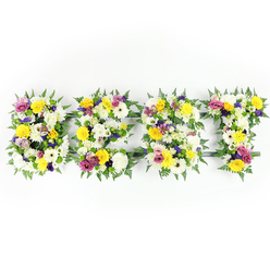 The first impression is of balance between colour and memory: four garden-shaped letters, lovingly sculpted and densely composed, sit against a serene white backdrop and read as a single, elegant statement. Warm, sunny yellows - rendered by roses and gerbera daisies - and crisp white chrysanthemums form the visual foundation, like captured daylight held in petals. Interspersed among them, soft lavender and mauve lisianthus or small chrysanthemums lend quiet depth, while bright magenta-pink spray roses or carnations add immediate, affectionate punctuation. Emerald-green fern fronds frame each letter, their soft blades blurring edges and giving the composition a gentle, organic silhouette.

The florist's craft is visible in the close packing of blooms and in the small, textured clusters of light green and white filler that add dimension and resilience to the surface. A subtle dark-green or metal armature peeks through in places - most noticeably where horizontal bars meet vertical stems - a reminder of the careful engineering required to keep large floral lettering upright and secure. Even, studio-style lighting highlights the fresh sheen of petals and the layered shadows between blooms, while suggesting the scent of warm roses tempered by green foliage.

This arrangement reads as a tender, uplifting tribute that brings calm and beauty to solemn moments. Prepared in a New Barnet workshop familiar with local services around Victoria Road and Oakleigh Park, it's the sort of handcrafted floral lettering chosen to honour a life, mark a farewell, or send a lasting message of love and remembrance.