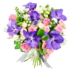 Presented against a pure white backdrop, this opulent bouquet appears almost to float, drawing full attention to the interplay of colour and texture crafted by a skilled New Barnet florist. The eye is immediately drawn to several large Vanda orchids, their petals a rich blend of royal purple and inky blue, intricately patterned with pale speckles and fine veins that seem to map out delicate constellations. Cradling these bold tropical blooms is a generous halo of pink roses, from tight, promising buds to fully opened blossoms with layered, blush-toned petals that suggest softness at a single touch. Creamy white spray roses are tucked between them, forming little pockets of light and adding a romantic, vintage charm. Scattered among the main flowers, tiny white starry fillers and clusters of round white hypericum berries introduce subtle movement and a fresh, almost dewy feeling, like a walk through the gardens around Oakhill Park after rain. Soft, silvery dusty miller leaves bring a cool, tactile contrast, their velvety surfaces playing gently against the smooth, glossy dark green foliage that frames and supports the design. The stems are tied with a luminous silver-lilac ribbon, sheer and slightly iridescent, pooling softly at the base and uniting the purples and pastels. The overall composition feels celebratory yet thoughtful, ideal for sending love on an anniversary, congratulating a new home near New Barnet station, or simply adding a touch of refined beauty to a dining table as evening light pours in.