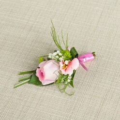 This exquisitely arranged floral boutonniere, carefully positioned on a textural linen reminiscent of New Barnet's quaint home interiors, embodies the artistry and attention to detail that local celebrations deserve. The centerpiece-a velvety pale pink rose-furls tightly in gentle spirals, holding a sense of joyful anticipation much like the first bloom of spring along the High Street. Paired with it, a delicate bloom reminiscent of light peach alstroemeria unfurls softly, its throat brushed with subtle golden veins and fine markings, adding intrigue and vibrancy. Puffs of baby's breath impart a dreamy lift, echoing the fresh air of surrounding Barnet parks, while vivid green cushion-like mums lend playful texture and a hint of woodland vitality. Lush green foliage flows outward, from spiky blades to gracefully folded leaves, structured to both frame and support the composition. Wrapping the base, a vivid fuchsia pink satin ribbon is tied into a tidy bow, its sheen catching gentle light and infusing the display with festivity and warmth. The arrangement's delicate blooms and foliage are set off by a coarse, neutral fabric that grounds the palette, highlighting the freshness and thoughtful assembly. Ideal for a groom or guest attending a wedding or prom in New Barnet, this boutonniere evokes a sense of romantic celebration, local pride, and the handmade touch of an experienced florist.