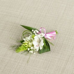 On a pale beige, linen-like background, a single, thoughtfully styled boutonniere rests as though just finished on a florist's bench in New Barnet, its details crisp and lovingly arranged. The focal point is a white alstroemeria bloom, sometimes called a Peruvian lily, fully open so that its broad petals fan outward with an almost papery softness. Near the base of each petal, fine reddish-brown streaks and speckles create subtle patterns that draw the eye toward the flower's centre, where its stamens rise delicately. Tucked just to the left, a vivid cone of lime-green buds, likely an Ornithogalum cluster, stands upright with tightly packed, scale-like segments, offering a modern, architectural contrast to the more romantic lily. Around these central elements, sprigs of feathery white baby's breath float like tiny stars, providing a misty, cloud-like texture. The greenery is carefully layered: bold, dark green leaves form a solid backdrop, while thin, bright green grasses and slender fronds weave through, introducing gentle curves and a sense of light movement, as if stirred by a Barnet breeze coming off nearby Oakhill Park. At the right edge, the stems are bound together with a smooth, satin ribbon in a clear, bright pink, tied into a neat little bow that adds a joyful, celebratory accent. The overall mood is calm, fresh, and quietly romantic, ideal for a groom or prom guest who wants a classic floral touch with a slightly contemporary twist, crafted in the style you might expect from an experienced New Barnet wedding florist.