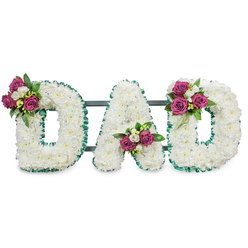 A carefully crafted memorial arrangement reads DAD in large, sculpted letters, each letter entirely cloaked in a cushion of immaculate white chrysanthemums that form smooth, cloud-like surfaces against a plain white studio background. The tactile quality of the flowers is immediate: tiny rounded florets packed closely to erase stems and filler, producing a serene, uninterrupted field of white that speaks of purity and quiet respect. Each letter is crisply outlined with a pleated emerald green ribbon, its cool tone adding a formal, evergreen frame that heightens the visual clarity of the typography. Thoughtful clusters of deep fuchsia to magenta roses sit at purposeful anchor points - upper left of the first D, tucked into the lower central V of the A, and on the upper curve of the final D. Interspersed white freesias and glossy dark green leaves lift the colour story and introduce a gentle fragrance, so the overall impression is both refined and intimate. A low-profile dark green support bar runs behind the letters to give structure without distracting from the floral surface, indicating the piece is meant to stand at a service or beside a coffin. Light is neutral and even, bringing out texture rather than shadow, and the arrangement radiates a calm dignity. As someone who arranges tributes for families around New Barnet and nearby Oakleigh Road, I picture this piece settling quietly in a chapel or laid with care at a graveside, offering a clear, personal farewell for a much-loved father.