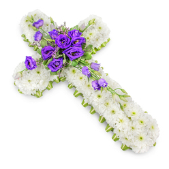 A traditional Christian cross made from flowers lies quietly against a pure white background, its form evoking the gentle stillness of a chapel near New Barnet High Street. The entire cross is composed of hundreds of fresh white chrysanthemums, each delicate bloom set closely beside the next to build a smooth, pillowy surface of petals. Their crisp white colour suggests purity and peace, while the faint green eyes at the centre of each flower lend a soft, natural variation to the design. Neatly tracing the perimeter of the cross is a slim lime-green ribbon, catching the light and creating a clear outline that accentuates the shape, much like the bright edges of new leaves in Oakhill Park in spring. At the heart of the cross, where the arms meet, sits an elegant cluster of deep purple lisianthus. These velvety blooms, layered and full, introduce a rich, regal note that conveys reverence and respect, their cool tones contrasting beautifully with the white beneath. Among them are wisps of green foliage and a scattering of small buds, lending the arrangement a sense of life unfolding even in moments of goodbye. A few lisianthus blooms and buds gently trail downward along the lower arm of the cross, adding movement, as though the flowers are quietly leaning towards the memory of the person they honour. Photographed from slightly above, the cross casts a soft shadow that makes it appear as if it is resting lightly on a table in a peaceful New Barnet chapel. This floral tribute is crafted to bring solace at a funeral, wake, or graveside service, offering a calm expression of faith, love, and remembrance.