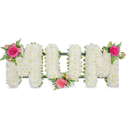 The image shows a traditional "MUM" funeral tribute, the three letters arranged in a neat line and photographed against a clean, white studio-style background so that nothing distracts from the flowers. Each capital letter is formed from a sturdy frame and then densely covered with countless white chrysanthemum heads, their petals overlapping to make a plush, slightly domed texture reminiscent of soft padding or a down-filled cushion. Around the base of the letters runs a narrow band of dark green, most likely ribbon fixed to the frame, which subtly outlines the shapes and hints at the craftsmanship behind the design. To soften the pure white, the florist has placed three matching accent clusters: one on the top left of the first M, one nestled in the lower centre of the U, and one on the top right of the final M. In each, a bold fuchsia rose or garden-style bloom is surrounded by smaller blush and mid-pink roses, partially open buds, and airy fern fronds that curl lightly over the chrysanthemums. The pink tones are warm without being bright, ideal for conveying love and gratitude, while the ferns bring a gentle woodland freshness. You can almost imagine the quiet of a chapel in New Barnet, or a reflective moment at New Southgate Cemetery, with this tribute resting near the coffin as family and friends say goodbye. The design feels deliberately personal, created to celebrate a mother's life with dignity, softness, and a clear, heartfelt message spelled out in flowers.