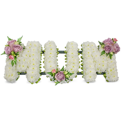 This carefully composed floral tribute spells out MUM in bold capital letters, each character densely covered in crisp white spray chrysanthemums so the surface appears pillowy and immaculate against a bright white studio background. The texture of the tiny chrysanthemum heads creates a gentle, cloud-soft finish that reads as dignified and serene, an emblem of purity and lasting memory. Three clusters of muted lavender roses and soft pink rosebuds punctuate the arrangement: one accenting the upper left arm of the first M, another nested in the U's lower curve, and a final grouping highlighting the upper right arm of the last M; the roses alternate between open blooms and closed buds, introducing a tender rhythm of life and recollection. Interspersed fern fronds and fresh green leaves add cool, vertical accents and a subdued countryside freshness reminiscent of local hedgerows around Station Road and Brunswick Park. A discreet dark green structural base-likely ribbon or moss wrapped around floral foam-traces the bottom edge of each letter and keeps the form unified while remaining almost hidden beneath the blooms. In soft, diffused lighting the arrangement radiates a hush of comfort and restraint, its faintly floral scent carried on the air. Prepared by experienced hands in our New Barnet workshop, Flowers New Barnet presents this design as a traditional and respectful funeral tribute suitable for services near New Barnet station, local chapels or graveside dedications.