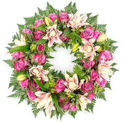 A richly detailed circular floral wreath, designed as a tender tribute, is presented against a spotless white backdrop so that every nuance of colour and foliage can be clearly seen, much like it would appear before being delivered to a solemn service in New Barnet. The wreath's structure is completely hidden beneath a mass of flowers and greenery, creating a soft, living ring with no hard edges. Dominant throughout are roses in jewel-like tones of fuchsia and magenta, balanced with gentler pinks; some blooms are tightly wrapped in anticipation, while others are fully opened, revealing layered, velvety petals that seem almost touchable. Nestled between them, generous double lilies span outward with broad petals in creamy white, blush pink, and pale peach, some with faint streaks or freckles of deeper colour, and a few buds stand tall in fresh lime-green, adding a sense of movement and time. Encircling and weaving through the flowers is an abundance of deep green foliage: fine, feathery fern fronds soften the outer ring, while sturdy, glossy leaves shape the inner structure and cradle each blossom. The white background lends a serene, almost chapel-like atmosphere, while the interplay of intense pinks and cool greens offers both warmth and calm. This carefully composed wreath feels appropriate for a final farewell at local New Barnet chapels, memorials near Oakleigh Park, or quiet gatherings at home, expressing sympathy, remembrance, and enduring affection through its thoughtful balance of colour and form.
