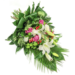 This lush and flowing floral tribute reflects the tranquil beauty found in the heart of New Barnet. Set diagonally against a stark white field, the arrangement effortlessly captures both elegance and heartfelt emotion, designed to provide solace during times of loss. Large, trumpet-shaped white lilies command attention with their serene presence-some petals splayed wide to reveal golden dusted stamens, others cupped with gentle promise, radiating a sweet, comforting scent reminiscent of early morning walks through leafy suburban streets. Velvet-petaled pink and deep fuchsia roses unfurl gracefully, their warmth enriched by the arrangement's gentle nod to remembrance and enduring love. Between the blooms, frilled white carnations add airy texture, setting a gentle rhythm. Distinct spheres of vibrant green santini chrysanthemums glow amid the greenery, their moss-like texture conjuring images of tranquil gardens and peaceful corners of Victoria Recreation Ground. Vivid red hypericum berries glint among the foliage, offering cheerful contrast and highlighting the bouquet's rich dimension. The abundance of foliage-layers of glossy, dark green leaves, some artfully folded, others left softly trailing-supports the cascading shape and infuses the display with a sense of natural abundance. Slender palm fronds and lighter, feathered leaves introduce elegant movement, like a gentle breeze passing through High Road on a quiet afternoon. This composition conveys serenity, dignity, and heartfelt sympathy, perfect as a funeral spray or memorial tribute delivered to families throughout New Barnet. Every detail speaks of skilled hands and local care, ensuring a fitting and graceful expression of respect.