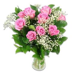 A softly lit photograph shows a classic pink rose and baby's breath arrangement, poised in a clear glass vase against a flawless white backdrop, like a little moment of calm joy brought indoors for a New Barnet nursery. Around a dozen roses form the heart of the bouquet, their petals unfolding in gentle layers of pastel and medium pink, some blooms still slightly cupped as if just opening to the day, others fully expanded with velvety whorls drawing the eye toward their centers. Misty clusters of white baby's breath weave through the roses, their tiny blossoms dotted delicately along fine green stems, giving the impression of a light, cloud-like veil floating among the larger blooms. Deep green foliage frames the arrangement, each leaf slightly glossy, suggesting freshness and careful conditioning in the florist's studio just off the High Road. The stems, visible through the transparent vase, stand in clean water that catches the light with a faint, reflective shimmer, underscoring the sense of purity and new beginnings. The bouquet has a rounded, balanced shape that feels thoughtfully composed rather than rigid, the flowers leaning toward each other in a natural, companionable way. This tender mix of pink and white would sit beautifully on a side table by a cot in a home near Victoria Park, or as a welcoming gift on the kitchen counter when family and friends stop by to meet a newborn. The overall feeling is one of gentle celebration, ideal for baby showers, naming days, or any heartfelt occasion linked to new life and soft, loving emotions.