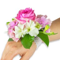This elegant wrist corsage is photographed on a left forearm of light-to-medium skin tone against a clean white field, its design speaking plainly of refined celebration. Central to the piece is a saturated hot-fuchsia rose, petals unfurling in a dense, velvet-like rosette that anchors the entire arrangement with rich colour and a hint of classic romance. Nestled around that rose are soft blush-pink hydrangea clusters, each tiny floret lending a puffy, cloud-like texture that contrasts with the rose's more structural form. White alstroemeria - Peruvian lilies - are artfully interspersed, their smooth petals and subtle pale-green streaking providing a crisp, luminous counterpoint. On the right edge a small gathering of pale green alstroemeria buds and a few minute, nearly closed pink blossoms create a sense of movement and promise, as though the corsage might continue to open through the evening. Broad, deep emerald leaves frame the flowers, their polished surfaces providing sculptural support and visual contrast. Securing this wearable bouquet is a delicate bracelet made from multiple strands of tiny, pearly beads; the pearls sit close to the skin, lending a vintage-modern fusion that readies the piece for weddings, proms, or milestone nights. The lighting is soft and natural, revealing textures and subtle colour shifts without harsh shadows. As a local florist with hands-on experience in New Barnet, I would envision this corsage arriving at a celebration on Station Road or being chosen by someone strolling through Brunswick Park for a springtime occasion.