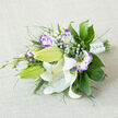 Stretched across an off-white, slightly coarse linen backdrop, this elegant bouquet displays the careful eye of a seasoned florist: large, pristine white Oriental lilies form the luminous center, their silky petals curving back to reveal pale yellow stamens and subtle brown-speckled throats, while several green buds speak of promises yet to open. Interspersed are lisianthus blooms - white at their heart that washes outward into vivid lilac and deep purple ruffled edges - and numerous half-open buds that add a painterly rhythm of color and tenderness. Airy clouds of Baby's Breath weave through the arrangement, offering a delicate, twinkling contrast to the more substantial blooms. The foliage is varied and abundant, from glossy, broad leaves to fine, feathery fronds and slender grassy spikes that introduce texture and soft architectural lines. A white satin ribbon binds the stems, punctuated with tiny pearl-like embellishments that catch light with a modest sparkle. The neutral linen ground lets the whites, greens, and purples sing, while a faint, spicy lily scent mingles with the sweet, clean scent of eustoma. Crafted for occasions that call for refined simplicity - bridal bouquets, intimate weddings, or a thoughtful anniversary gift - this piece also reflects local care; Flowers New Barnet prepares similar hand-tied bouquets for same-day delivery around New Barnet, near Station Road and the High Street, ensuring freshness and attentive presentation for every celebration.