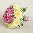 Set against a softly textured, oatmeal-coloured cloth that resembles fine hessian or natural linen, this hand-tied bouquet is captured from above so the viewer can admire its perfectly rounded symmetry. The arrangement is composed entirely of roses and delicate filler, divided almost like two halves of a sunrise: one side a sweep of vivid magenta-pink roses, the other side a glowing expanse of buttery, pale yellow blooms. Each rose is in full, luxurious bloom, with petals unfurling in tight spirals that give a sense of fullness and richness, as if the flowers have just arrived fresh from the morning markets that serve New Barnet and the surrounding Barnet High Street. Between the larger blossoms, airy sprays of white baby's breath thread their way through, creating a soft cloud-like effect that lightens the overall design and hints at traditional wedding styling. Subtle dark green foliage emerges at the edges, adding contrast and drawing the eye back into the heart of the bouquet. The stems are carefully bound and wrapped in glossy pink satin ribbon, which has a gentle sheen, and the handle is further embellished with a winding strand of tiny white pearls, giving the bouquet a refined, heirloom quality. This elegant design feels perfect for a New Barnet bride walking down the aisle at a local church, for an intimate civil ceremony near Hadley Common, or for a romantic gesture that celebrates enduring love. The colours and textures together evoke softness, warmth, and a quiet joy, like a promise held tenderly in both hands.