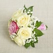 Balanced delicately across a softly textured cream fabric, this exquisite bridesmaid or small bridal bouquet captures the subtle elegance that defines New Barnet's signature floral designs. Central to the arrangement are five creamy white roses, their petals unfurling with a lush, layered beauty that seems almost velvety. Nestled slightly off-centre sits a single, radiant magenta rose whose vivid hue draws the eye and infuses the arrangement with cheerful contrast-mirroring the unexpected bursts of colour that grace the gardens near Victoria Recreation Ground. Wispy sprays of white baby's breath, artfully interlaced among the blooms, impart a sense of delicacy and airiness, pairing beautifully with the sparse yet striking deep green foliage that frames the bouquet. The carefully wrapped stems-secured with a textured, fuchsia pink ribbon and adorned with winding strands of glowing white pearls-impart a sense of refined craftsmanship. Illuminated by gentle, natural light, every petal, leaf, and embellishment is bathed in a soft radiance, reflecting the promise and joy found at celebrations throughout New Barnet. Whether held by a bride, carried by a bridesmaid, or offered as a celebratory flourish, this bouquet expresses the timeless romance and community pride unique to this North London neighbourhood.