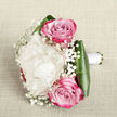 Captured from a gently elevated angle, this romantic bouquet lies against a pale, linen-like fabric that glows softly, as if lit by calm afternoon light drifting through a New Barnet window. At its center, a full-bodied creamy white peony unfurls layer upon layer of ruffled petals, forming a sumptuous, cloud-like blossom that immediately draws the eye. Embracing this focal flower are two elegant pink roses, one slightly above and the other just below, their petals coiling inward in a classic spiral. The roses' colour shifts from a tender blush at the heart to a more intense fuchsia or magenta along the outermost petals, giving the arrangement a beautiful sense of movement and contrast. Between these statement blooms, fine threads of white baby's breath weave in and out, each tiny cluster resembling soft snowflakes suspended in the air, lending a floaty, ethereal charm. Surrounding the base, deep green aspidistra-style leaves curve protectively, their glossy finish providing structure and a striking frame for the paler flowers above. The stems are carefully bound with smooth white satin ribbon, suggesting a design crafted to be held down the aisle or presented as a heartfelt gift. The bouquet feels refined yet natural, the kind of arrangement a New Barnet couple might choose for a registry office ceremony near High Barnet or a celebration overlooking the greenery of Oak Hill Park, reflecting both modern taste and traditional romance in every carefully placed stem.