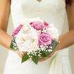 A romantic wedding bouquet is shown cradled in a bride's hands, the flowers arranged in a classic, compact dome that feels both luxurious and calm, as if echoing a peaceful New Barnet afternoon. At the centre, grand creamy peonies unfold in soft layers, their petals billowing like quiet whispers, each bloom full and velvety. Woven between them are roses in shades of dusty pink and gentle lavender, their buds still slightly tight, adding a sense of anticipation, like the moments before a ceremony at a local New Barnet hall or church. Wisps of gypsophila are scattered throughout the bouquet, peeking out in delicate white clusters that evoke purity and classic bridal charm, reminiscent of blossom clouds along Lyonsdown Road in spring. Shiny dark green foliage curls around the base, forming a natural cocoon that sets off the pastel tones and heightens the impression of softness. The stems are tidily wrapped, offering the bride a secure, intimate grip as she walks down the aisle, perhaps at a venue near Victoria Park or along the quiet streets towards High Barnet. The overall colour palette-creamy whites, muted pinks, and lilac-creates a tranquil mood, suggesting harmony and grace rather than drama. As a florist who knows the gentle, residential rhythm of New Barnet, this bouquet feels like a reflection of local weddings here: thoughtful, quietly elegant, and deeply personal. It's easy to imagine the fresh, lightly sweet scent following the bride through the day, leaving a lingering memory of love, serenity, and carefully curated beauty.
