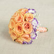 Captured from just above and laid horizontally on a textured, light beige linen backdrop, this bouquet feels like a quiet vow. The design's heart is a dense cluster of full-blown roses in warm peach and soft orange, each bloom opening in concentric spirals that create rich, velvety depth and a sense of abundance. Woven through them, white lisianthus tipped with a striking deep violet edge introduce a cool, contemporary punctuation-those ruffled rims read like ink on fine paper, sharpening the arrangement's palette. Wisps of baby's breath float among the larger flowers, their tiny white stars giving the bouquet a light, airy conversation between solidity and breath. The stems are finished in a satin ribbon of light peach-coral, visible toward the bottom right where a delicate strand of cream pearls wraps around the handle, lending a tactile shimmer and old-world refinement. Under soft daylight, petal textures and subtle colour transitions are gently revealed while the neutral fabric beneath adds warmth and tactile contrast. Speaking as a florist who knows New Barnet's quiet streets and small celebrations, I imagine this in the hands of someone emerging from Station Road toward Brunswick Park-an arrangement that reads as both timeless and personal, ideal for a wedding, anniversary, or intimate ceremony in the neighbourhood. The overall impression is romantic, elegant, and quietly celebratory, with a scent of warm roses and a whispered sophistication.