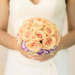 There is a soft, lyrical quality to this arrangement that suits a wedding morning perfectly: apricot roses are gathered in a symmetrical cluster at the centre, their cups unfolding in warm, sunlit tones like small, satin suns. Encircling them is a ring of purple-tipped and white lisianthus, their cool colours offering a graceful contrast that evokes twilight brushing a peach sky. Interwoven throughout is a delicate lattice of white baby's breath, fine and cloud-like, giving the bouquet a weightless air as if it might float away on a summer breeze. Light falls across the composition in gentle washes, highlighting petal veins and the tender curl of each rose while softening the lisianthus into pale, dreamy accents. The texture balance-creamy rose petals against the near-ethereal crispness of the filler-creates a bouquet that feels both refined and eminently wearable. I picture this piece being collected from Flowers New Barnet on Station Road for a ceremony close to New Barnet station, wrapped in simple cream paper with a ribbon to match; it travels well, arriving fresh and fragrant, ready to be paired with lace or a modern gown. The emotional note is timeless: celebration and promise contained in a hand-held composition, crafted to sit quietly at the centre of a day full of vows, laughter, and close family. The overall effect is elegant, calm, and confidently romantic-an heirloom feeling made for immediate joy.