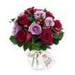 A richly hued, hand-styled bouquet of roses captured against a clean white backdrop, where deep crimson and velvety burgundy roses sit cheek-by-cheek with soft lavender and dusty purple blooms. The roses are fully open, their layered petals unfurling like satin, and the arrangement is dense and rounded so the eye reads a single, luxurious mass of colour. Dark green foliage-suggestive of Ruscus or Salal-tucks in between the heads, its glossy leaves adding sculptural depth and a cool, leafy scent that frames the roses. Scattered through the clusters are small, bright red-orange rose hips that catch the light with a slightly matte, rustic texture, offering an autumnal counterpoint to the roses' opulence. The stems are presented in an antique-style mercury glass vase: rounded at the base, tapering toward the rim, its mottled silvered surface reflecting tiny glints of studio light. Natural raffia or twine is tied around the neck for a handcrafted finish, and a small rectangular white tag hangs forward, blank of branding so the focus stays on the flowers. The overall mood is romantic and quietly luxurious-a bouquet that feels equally at home on an anniversary table or as a thoughtful delivery for someone needing comfort. Imagine holding it and breathing in the warm, honeyed scent of red roses against the cooler, powdery note of lavender petals, the berries adding a faint, earthy tang beneath. This image reads as fresh, premium floral work: careful composition, tactile contrasts, and a timeless palette that makes the arrangement suitable for special occasions or elegant home styling in and around New Barnet.