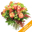 A vibrant, hand-tied autumn bouquet set against a clean white background, glowing with warm peach, coral and russet tones. At its heart are large, fully opened roses whose centers melt from soft apricot into deeper coral at the outer petals, their velvety spirals catching soft studio light. Scattered among the roses are bright orange and butter-yellow freesia, their delicate trumpets and unopened buds lifting the composition with elegant, fragrant notes. Dark glossy foliage and lighter chartreuse sprigs form a lush cradle beneath the blooms, while clusters of lime-green hypericum berries and tight-eyed green Santini chrysanthemums add lively texture and a refreshing counterpoint to the warm palette. Autumnal character comes from a few deep reddish-brown oak leaves, their lobed silhouettes tucked artfully through the stems to evoke fallen leaves and crisp walks in nearby Brunswick Park and Oak Hill Park. The bouquet's trimmed stems are gathered and tied with natural jute twine, ready for a vase on a mantle or a festival table. A bright diagonal orange banner with bold white letters reading FREE CHOCOLATE overlays the lower right corner of the image, indicating a promotional overlay. The overall effect is both luxurious and homespun - a bouquet that suggests the scent of earth and spice, a tactile mix of velvety petals and crisp leaves, and the quiet warmth of autumn afternoons in New Barnet.