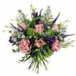 Captured in bright, even light against a clean white background, this bouquet radiates a gentle, romantic energy, as if just carried in from a New Barnet florist on a clear morning. The composition is a harmonious blend of rounded and linear forms: soft pastel pink roses open gradually across the arrangement, their petals unfurling in delicate, layered curls, some edged with slightly deeper pink that adds a natural, blushed warmth. Interspersed with them are voluminous carnations in tones of dusty rose and mauve, their frilled petals overlapping in rich, textural waves that give the bouquet a plush, almost cushion-like fullness. Rising through this soft mass of petals are slender, upright stems of Veronica in deep violet-blue, providing graceful height and a touch of contemporary flair. Tucked among the taller spires are clusters of purple lisianthus, their bell-shaped blooms and buds offering a velvety counterpoint to the roses' satiny sheen. Sprays of tiny, lavender-blue aster-style flowers run like threads through the design, creating a sense of airiness and light movement, as though the bouquet has just been gently turned in the hands. Around the flowers, a collar of varied foliage frames the colours, from bright chartreuse filler that almost glows, to cooler eucalyptus greens that soften the edges and echo the calm greenery of local streets near New Barnet station. The stems at the bottom are visible, trimmed to an even length and bound together in the classic hand-tied style, ready to slip into a favourite vase. The overall impression is of a thoughtfully crafted bouquet, perfect for expressing affection, offering comfort, or marking a special day in and around New Barnet.