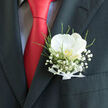 Set against the clean lines of a charcoal jacket and a bold red tie, this New Barnet pocket boutonnière feels like a small but powerful symbol of commitment and style. At its centre, a single white orchid blooms with serene confidence, its petals wide and gently curved, glowing with a creamy, almost pearly light. The inner throat of the flower holds a muted golden tone, like a secret warmth that only reveals itself on closer inspection. Around this focal bloom, clusters of baby's breath float like a soft cloud, each tiny flower adding an airy, romantic texture that calls to mind the delicate blossoms you might see in gardens near Victoria Park or along New Barnet's quiet residential streets. Wisps of fresh greenery weave through the design, their cool green shades and slender shapes bringing depth, dimension, and a hint of natural movement. At the base, a narrow white ribbon is folded into a neat bow, its satin sheen reflecting the care and precision of a practiced florist's hands. The overall effect is one of refined simplicity, the kind of boutonnière chosen thoughtfully for a wedding day, engagement celebration, or black-tie event in the local area. The contrast of the vivid red tie, the dark suit fabric, and the pristine orchid creates a sense of anticipation, like the moment just before walking down the aisle or greeting guests. Crafted with the quiet expertise you would expect from Flowers New Barnet, the piece speaks of love, ceremony, and the subtle elegance that turns a well-dressed outfit into a meaningful memory.