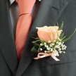 With an air of timeless elegance, this classic boutonniere graces the suit lapel of a local New Barnet gentleman, perhaps preparing for a wedding at a nearby church or a festive celebration in one of the area's leafy parks. At its heart, a single peach blush rose unfurls its buttery-soft petals, their gentle sheen catching the morning light much like dew on fresh grass near Monken Hadley Common. Encircling the central bloom, frothy clusters of baby's breath and slender, fresh-green fronds create a lively, textured frame, recalling the carefree grace of New Barnet's gardens at dawn. Nestled seamlessly against the finely structured charcoal suit, the matching satin ribbon bow in peach provides an understated accent that echoes the well-chosen necktie beneath. The fragrance is delicate-sweet, comforting, and fleeting, reminiscent of summer evenings just after rain. Here at Flowers New Barnet, every buttonhole is crafted not merely as a formality, but as a heartfelt marker of unity, joy, and beginnings. With each flourish of blossom and greenery, this arrangement becomes a meaningful emblem for life's most cherished events in the heart of our community.