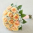 Elegance and tenderness come together in this New Barnet hand-tied bouquet, perfectly suited for weddings and moments of deep celebration. At its core, lush peach roses bloom in a tight, radiant embrace, each petal spiraling with a creamy blush and kissed by a hint of apricot at the center. Wisps of delicate gypsophila, soft as bridal lace, weave around the roses in airy clusters, amplifying their beauty without diminishing their gentle glow. Vibrant green leaves, polished and abundant, lend a foundation of freshness-a visual echo of the nearby green spaces that distinguish New Barnet. The stems are precisely tied in a peach-hued ribbon, meticulously dotted with little pearls in an elegant grid, their smooth, cool surfaces adding a tactile richness that trembles with quiet joy. The bouquet lies diagonally on a subtle, woven cream cloth, capturing the soft daylight that streams through local windows and highlighting every nuanced shade and detail. The light, sweet fragrance drifts upward, reminiscent of early spring walks along Park Road. Designed to evoke hope, comfort, and celebration, this bouquet channels the grace and anticipation found at life's most treasured moments in New Barnet.