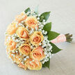 This hand-gathered bouquet speaks of gentle devotion: apricot-peach roses arranged in a rounded cluster, their silky petals layered tightly so each bloom feels plush and substantial. Between and above the roses, clusters of white gypsophila float like whispered notes, adding air and romantic weightlessness that lets the peach tones breathe. Rich emerald foliage-the leaves broad and slightly glossy-frames the composition, providing a lush, organic backbone that guides the eye around the bouquet and into its warm centre. The stems are neatly wrapped in a textured, blush peach ribbon studded with tiny pearls; the wrapping is both practical and ornamental, its tactile finish suggesting careful, practiced hands. Photographed in soft, diffuse light, the bouquet glows with muted highlights and gentle contrast, which reveals the roses' creamy undertones and the delicate filigree of the baby's breath without harshness. A subtle scent trail is implied: green, freshly cut foliage mingles with the sweet, true fragrance of roses and the faint, powdery whisper of gypsophila. As a local florist at Flowers New Barnet, I often think of this style for bridal parties walking along Victoria Road or couples celebrating anniversaries by Oak Hill Park-its restrained elegance suits both weddings and intimate milestones. The arrangement conveys warmth, composure, and hopeful anticipation; held close it becomes more than flowers, acting as a quiet, fragrant companion to a memorable day.
